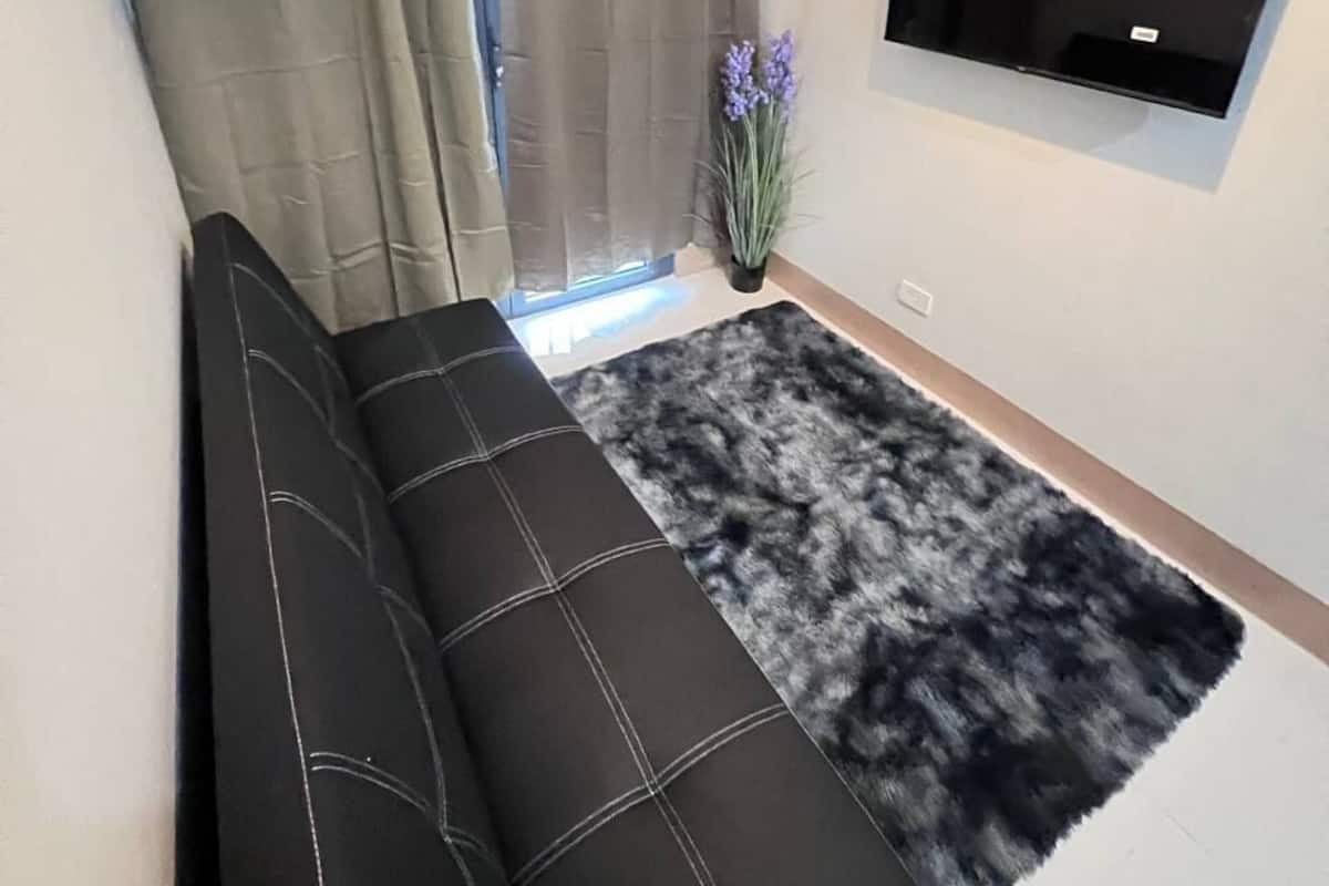 Ein modernes Wohnzimmer mit einer schwarzen Couch, einem Wand-Fernseher und einem Fenster mit Vorhängen.