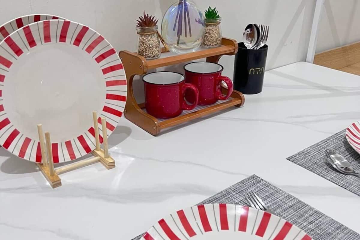 Una mesa de comedor preparada con platos a rayas, tazas rojas y un pequeño jarrón con flores.