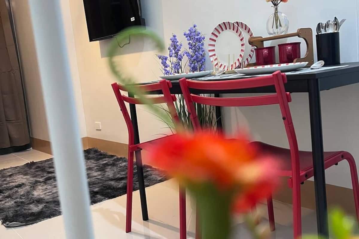 A dining area with a TV mounted on the wall, a table with red chairs, and a decorative mirror.