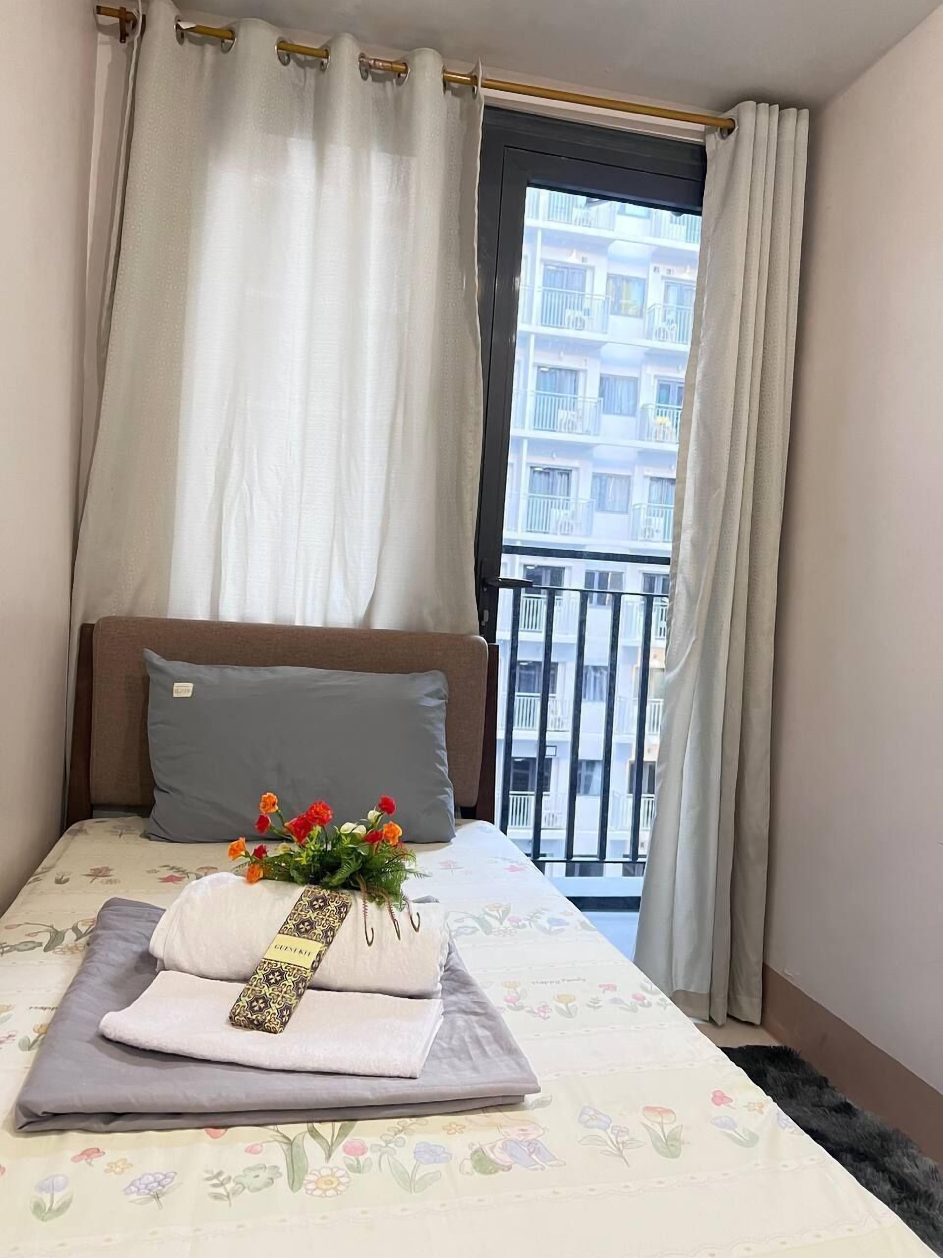 Una habitación de hotel con cama, ventana con cortinas, balcón y colcha estampada con motivos florales.