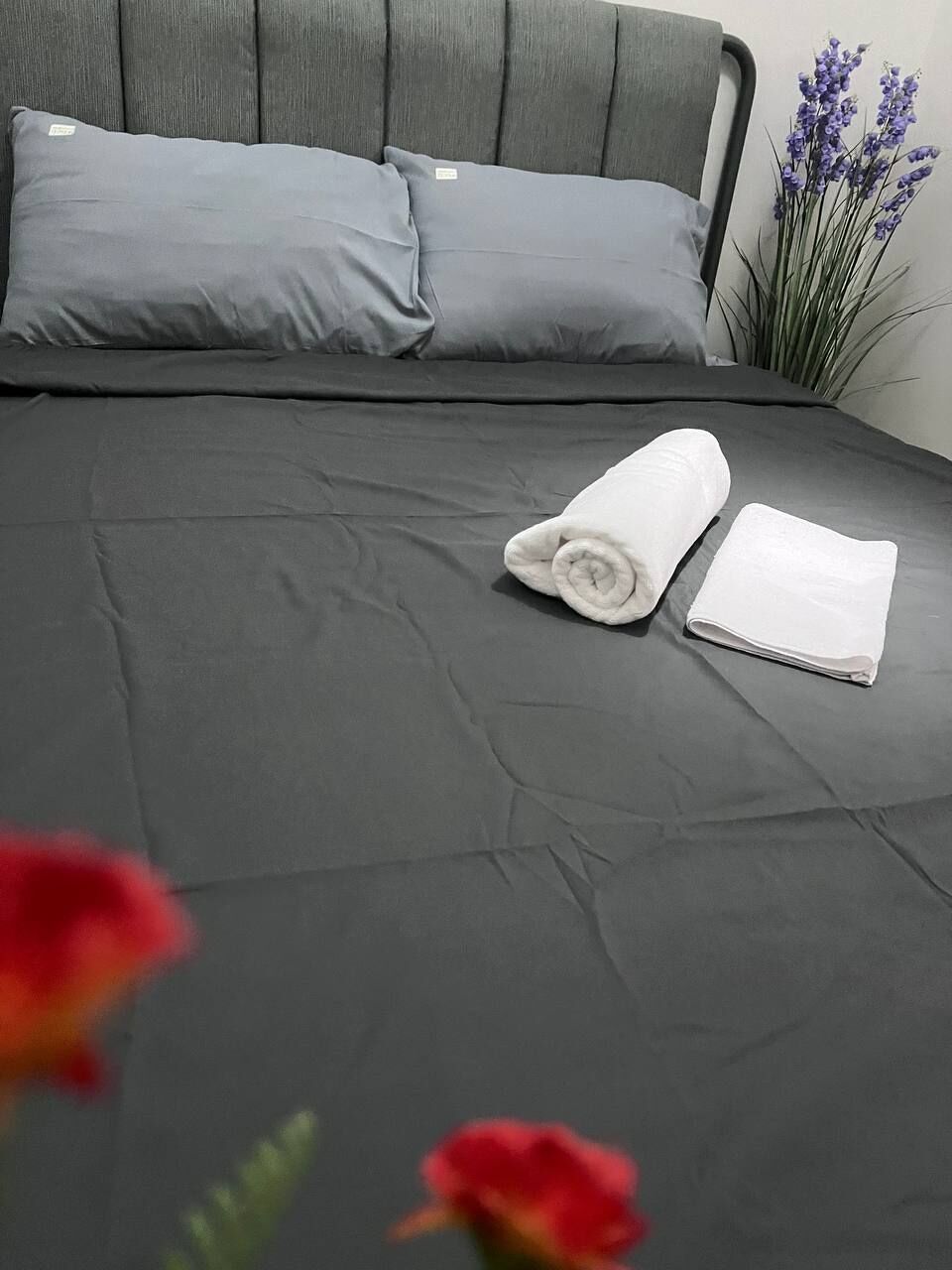 A neatly made bed with grey bedding and two rolled white towels.