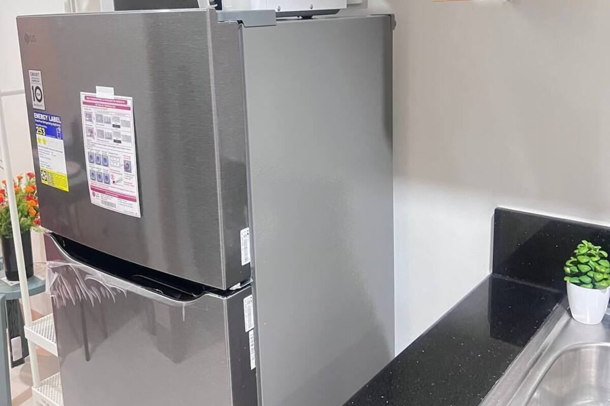 Un réfrigérateur en acier inoxydable doté d’une étiquette d’efficacité énergétique, un four à micro-ondes placé sur le dessus, et une petite plante en pot posée sur le plan de travail.