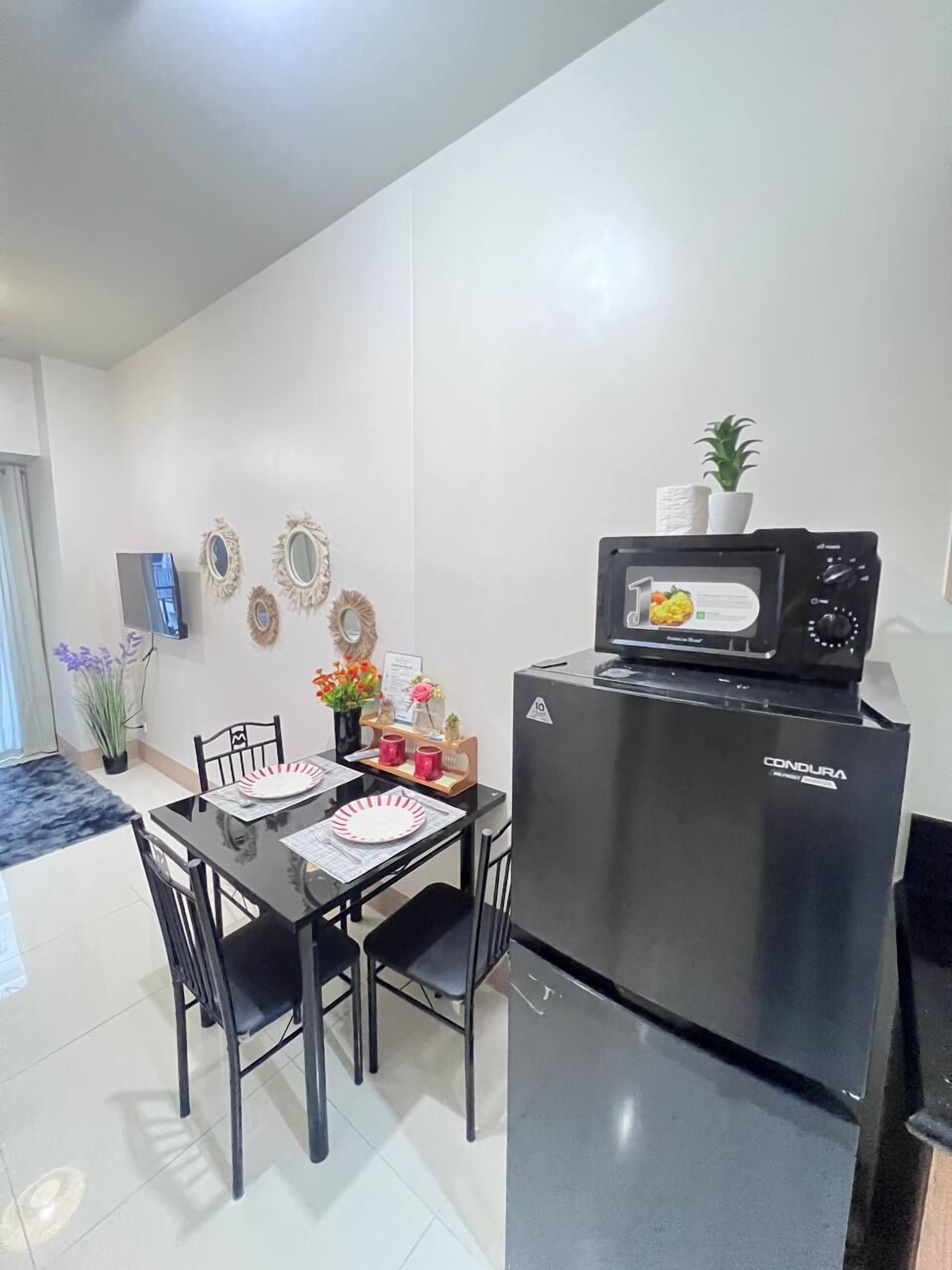 A compact kitchen with a black refrigerator, a microwave, and a dining table with chairs.