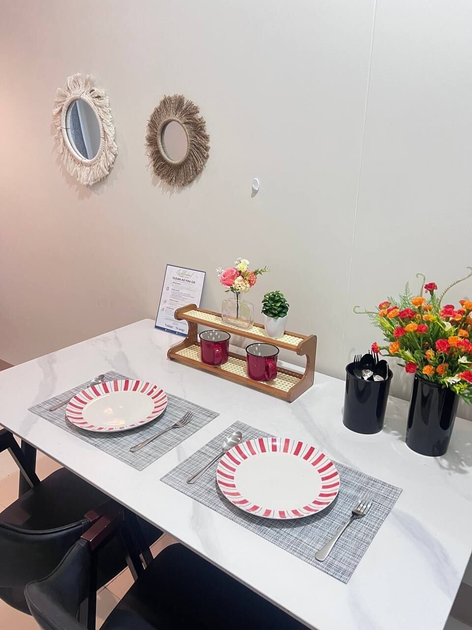 A dining table with two plates, a menu, a vase with flowers, and a small plant.