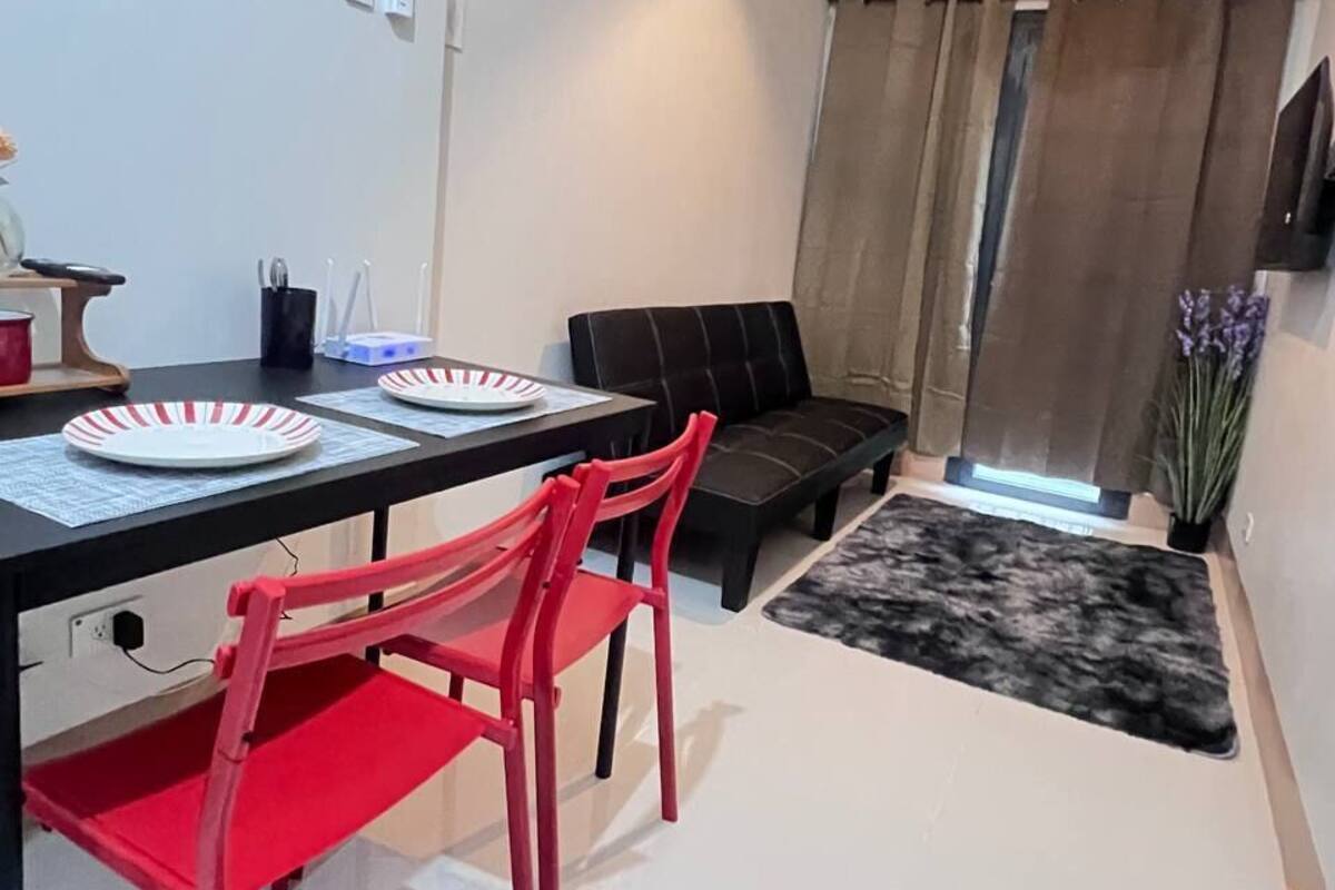 Una sala de estar moderna con comedor, que incluye un sofá negro, sillas rojas, un tapete negro y una lámpara de techo.