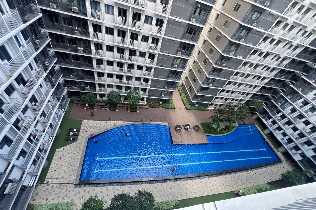 Un edificio alto con numerosi balconi, una piscina centrale e aree verdi circostanti.