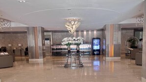 Um hall amplo com design moderno, com um balcão de recepção, um grande lustre e uma tela digital exibindo informações.