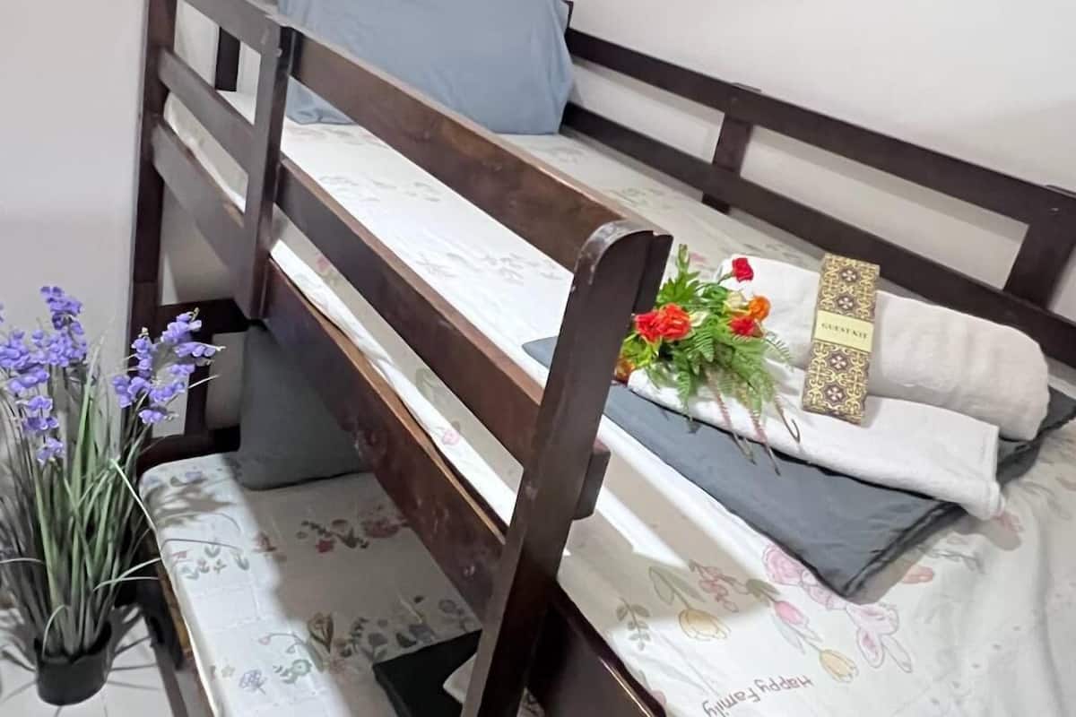 Una cama litera con una colcha de estampado floral, una almohada azul y una almohada decorativa con etiqueta 'GUESTFIND'.