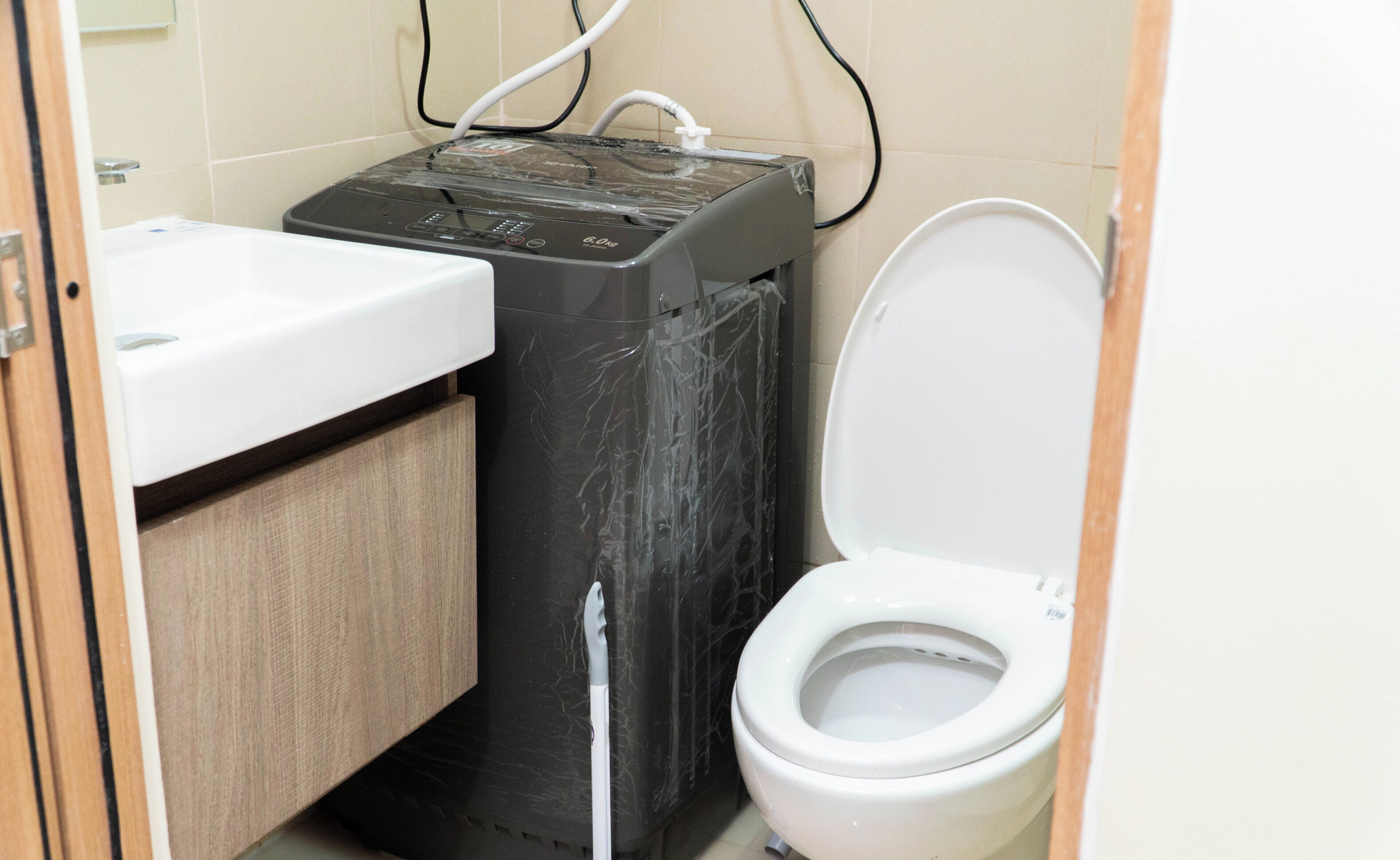 Un baño pequeño con un lavamanos blanco, un inodoro negro y un calentador eléctrico negro.