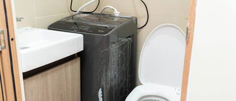 Un baño pequeño con un lavamanos blanco, un inodoro negro y un calentador eléctrico negro.