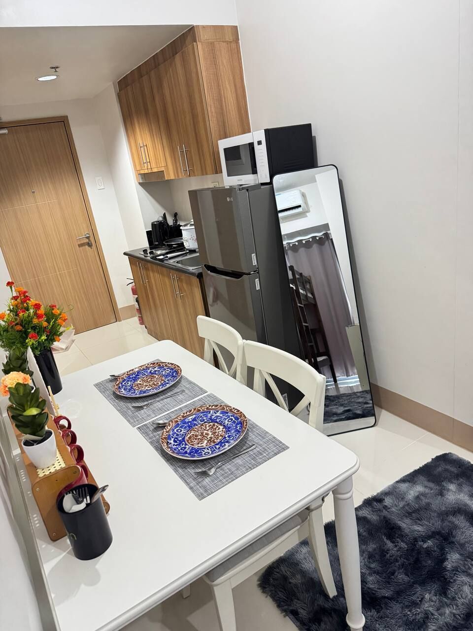 A modern kitchen with wooden cabinets, a black refrigerator, a microwave, and a dining table set with plates and utensils.