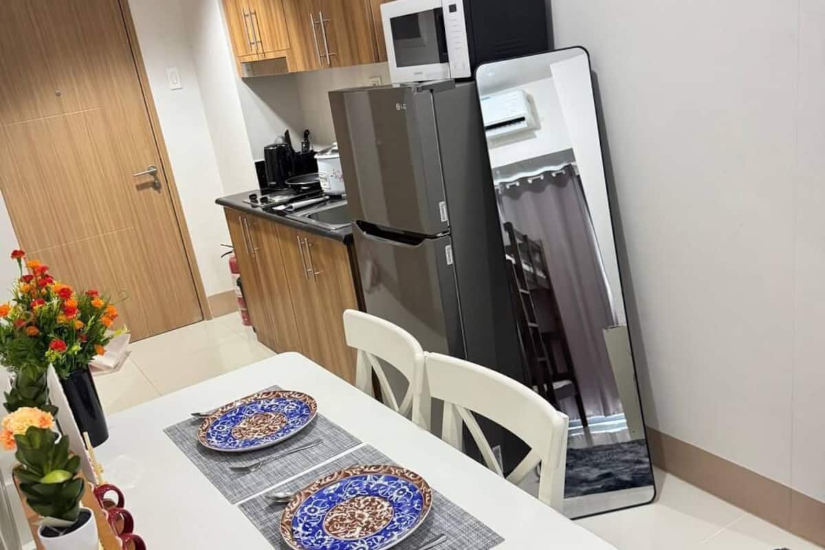 A modern kitchen with wooden cabinets, a black refrigerator, a microwave, and a dining table set with plates and utensils.