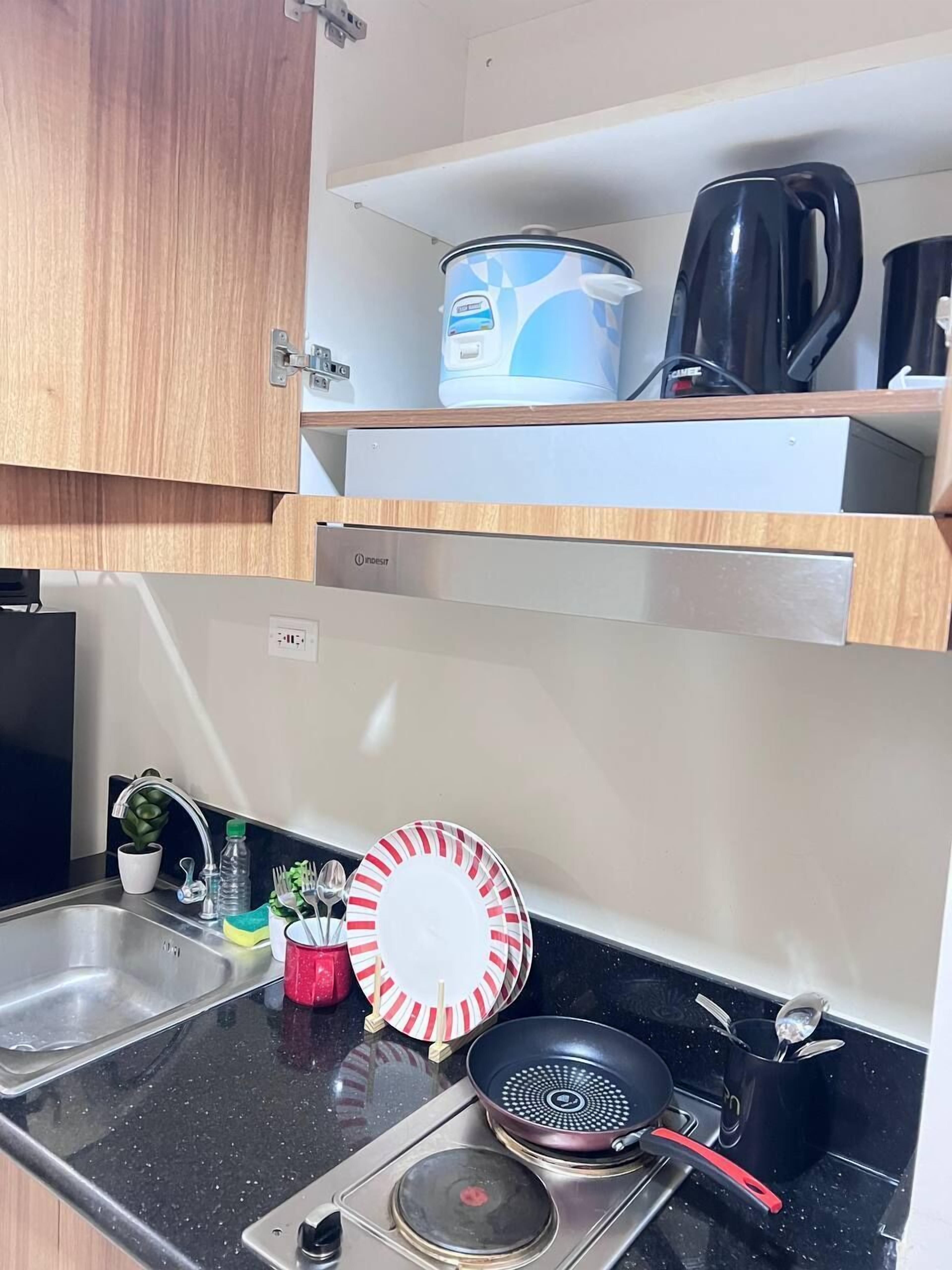 A compact kitchenette with a sink, a stove, a frying pan, a kettle, and a coffee maker.