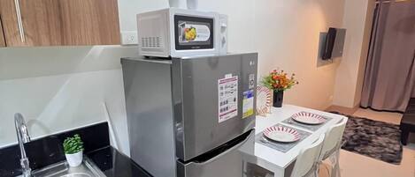 A modern kitchen with a stainless steel refrigerator, a microwave, and a sink. There is a dining area with a table and chairs.