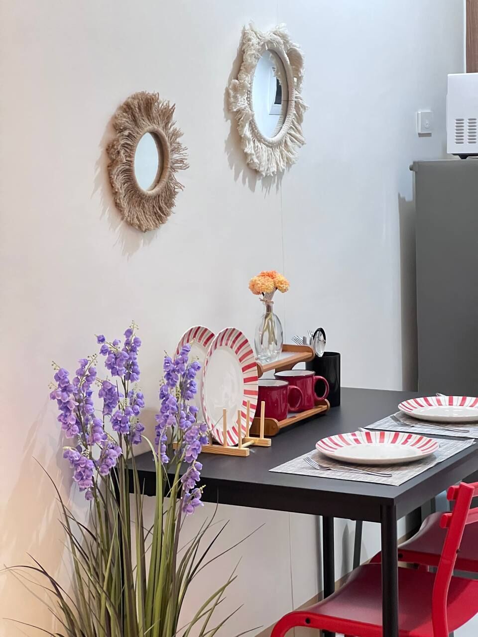 A dining area with a table set for two, featuring striped plates, a vase with flowers, and a mirror on the wall.
