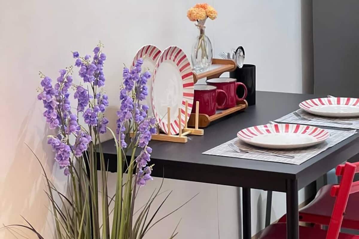 A dining area with a table set for two, featuring striped plates, a vase with flowers, and a mirror on the wall.