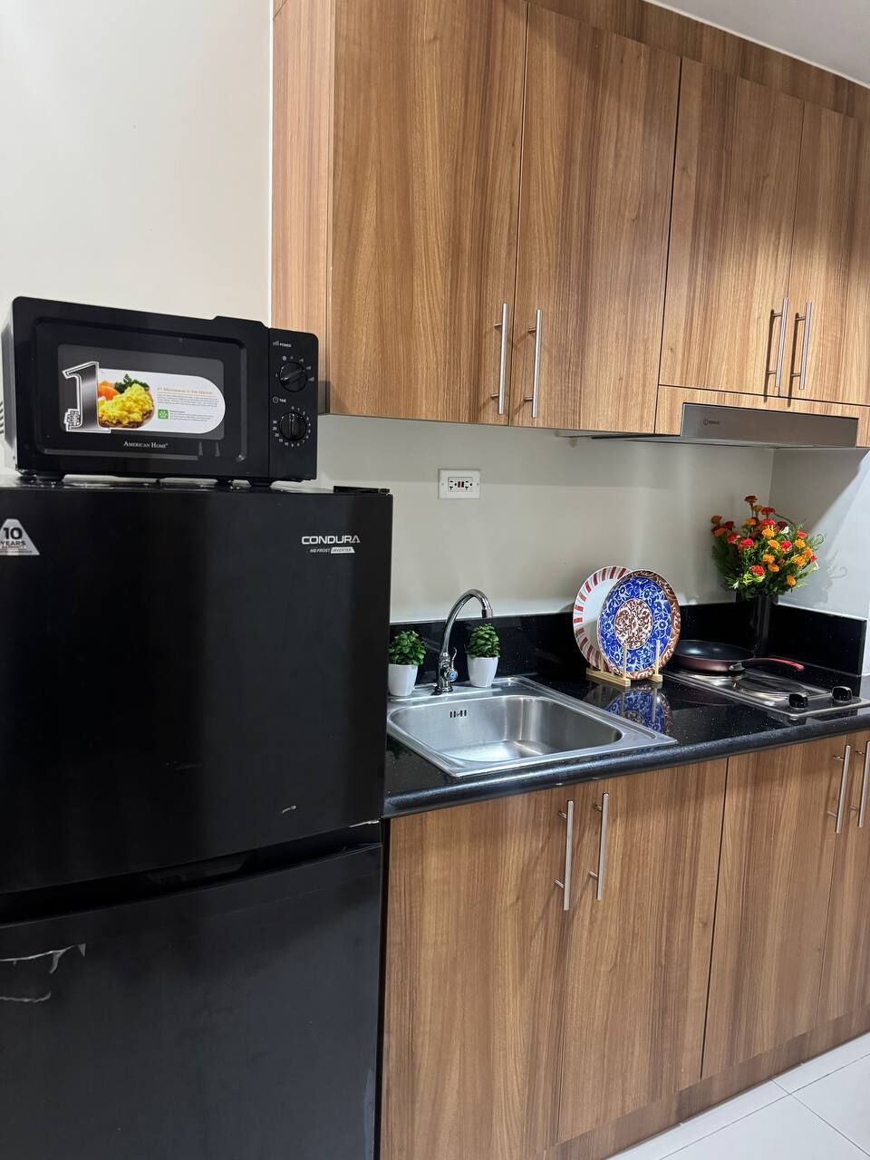 A kitchen with a black refrigerator, a microwave, a sink, and wooden cabinets.