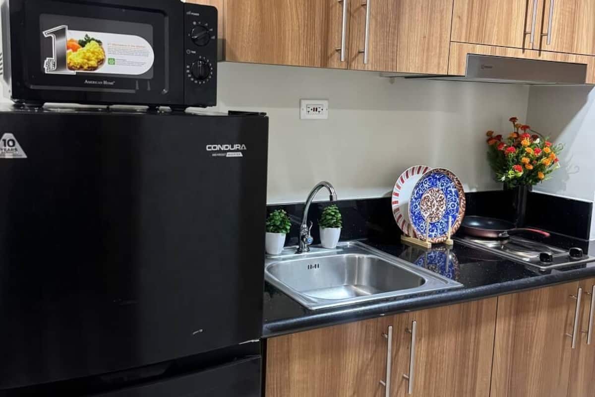 A kitchen with a black refrigerator, a microwave, a sink, and wooden cabinets.