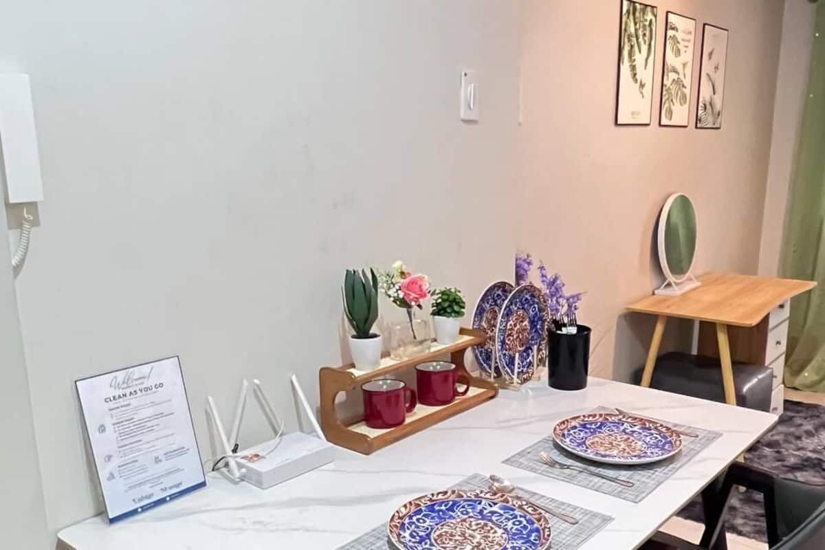 Un coin repas avec une table blanche, deux chaises, une petite plante, un tableau encadré et un panneau accroché au mur.