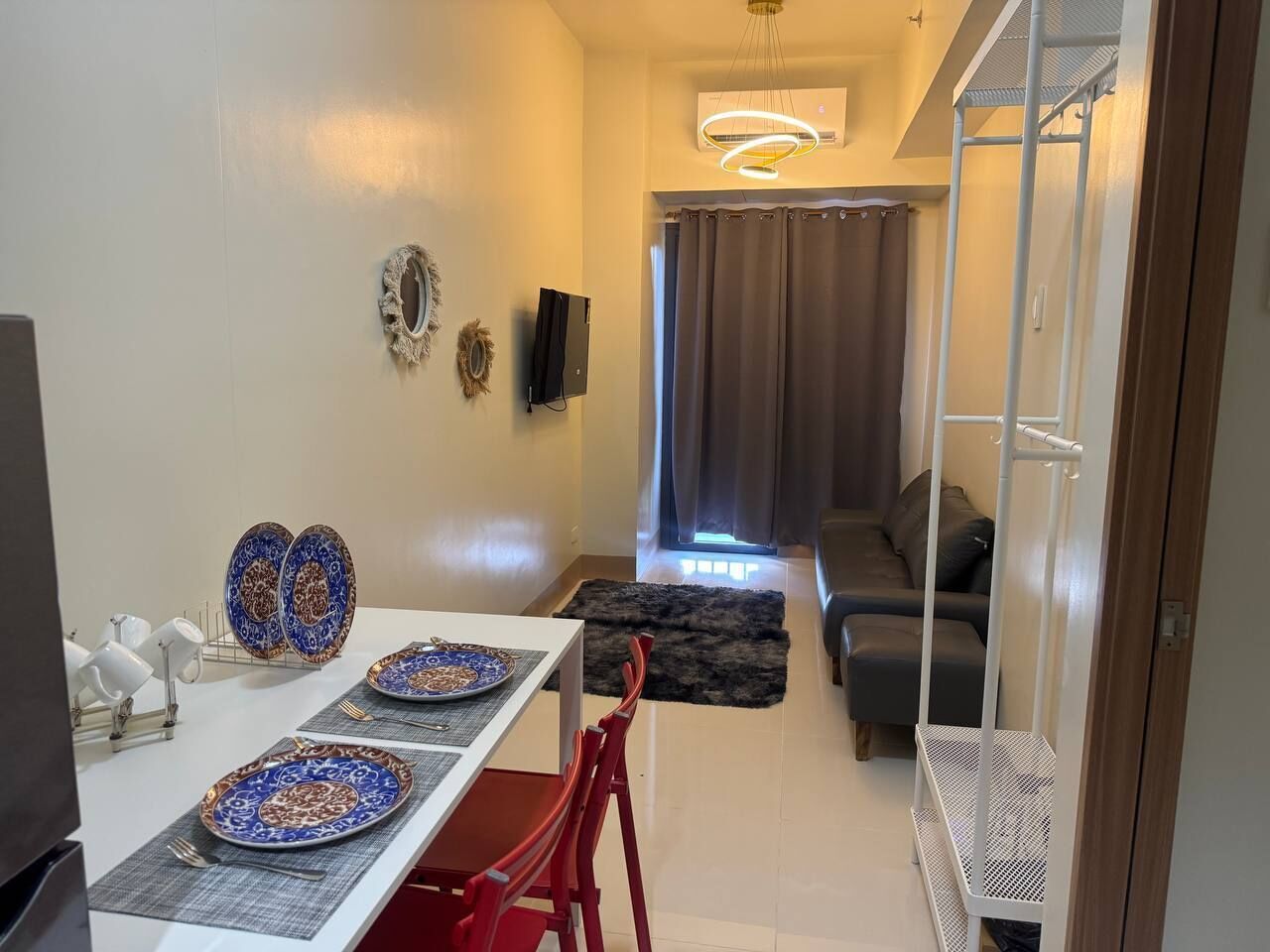 Un comedor con una mesa preparada para dos personas, un sofá al fondo y un ventilador de techo blanco.