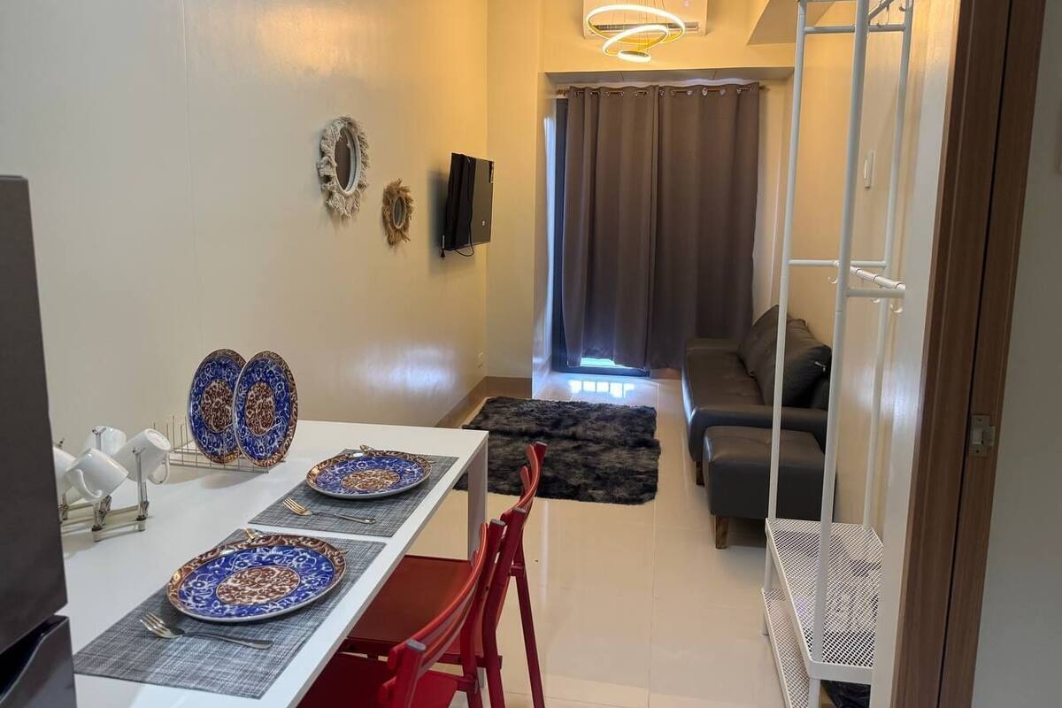 Un comedor con una mesa preparada para dos personas, un sofá al fondo y un ventilador de techo blanco.