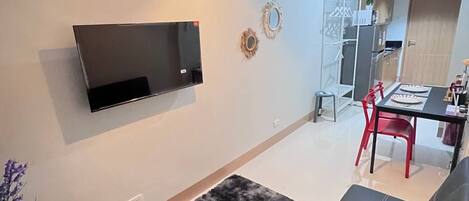 Un salon moderne avec un canapé noir, un téléviseur fixé au mur, un tapis noir et blanc et un coin repas avec des chaises rouges.