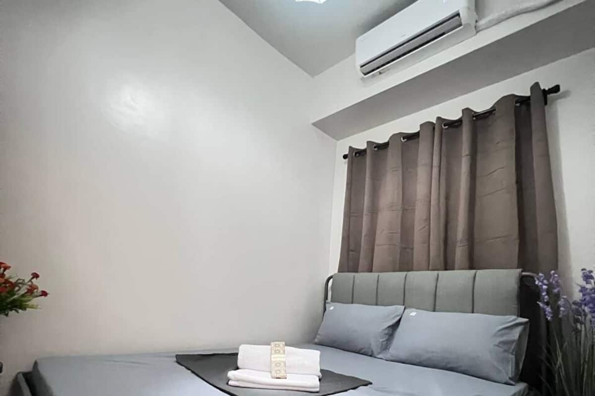 Un lit simple avec une tête de lit, un climatiseur fixé au mur et une fenêtre avec des rideaux.
