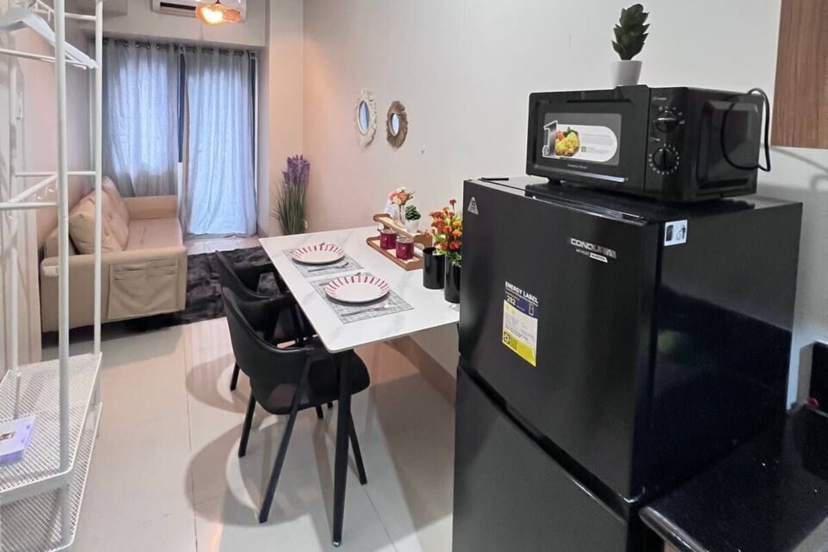 A compact kitchen with a refrigerator, microwave, and dining table set for two.