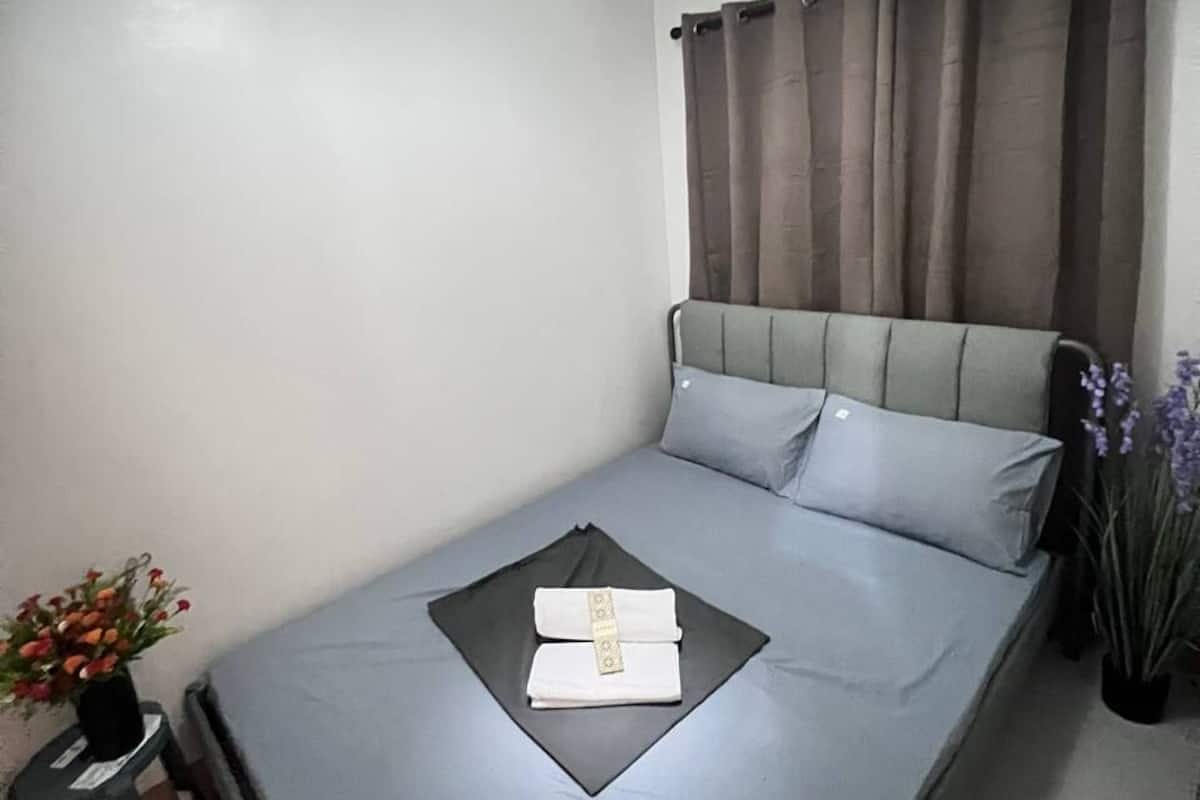Una cama bien hecha con una toalla doblada y un pequeño adorno sobre un tapete oscuro.