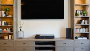 Un soggiorno moderno con una grande TV a schermo piatto montata a parete, circondata da scaffalature a incasso con libri e oggetti decorativi.