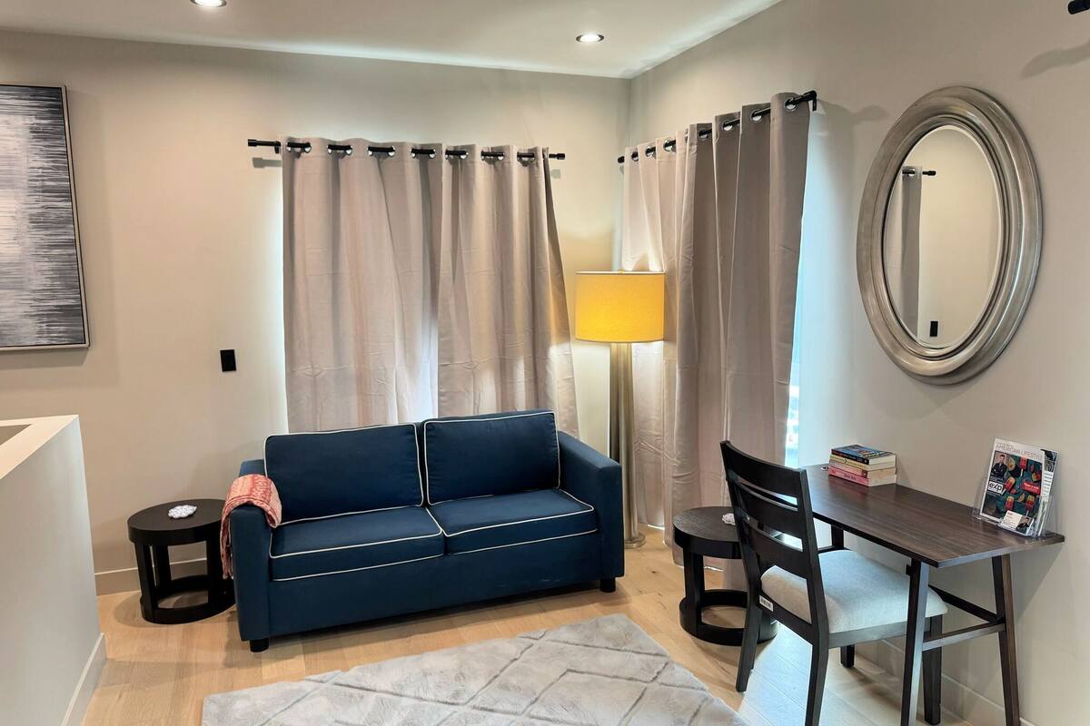 Ein Wohnzimmer mit einem dunkelblauen Sofa, einem kleinen runden Tisch, einem Sessel, einer Lampe und einem Spiegel an der Wand.