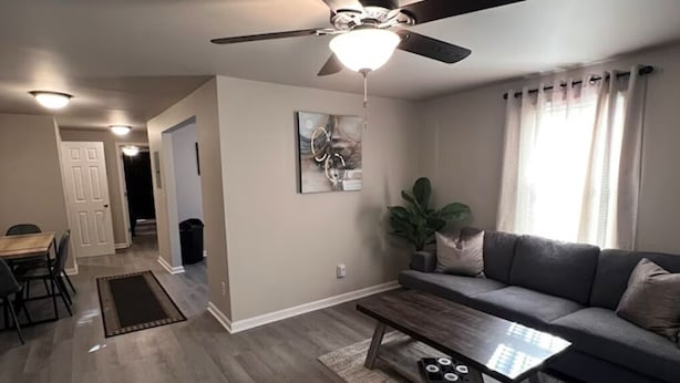 Una sala de estar moderna con un ventilador de techo, un comedor con mesa y sillas, y un sofá gris con una mesita de centro.