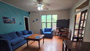 Uma sala de estar com um sofá azul, uma mesa de centro de madeira e uma TV sobre um móvel de madeira.