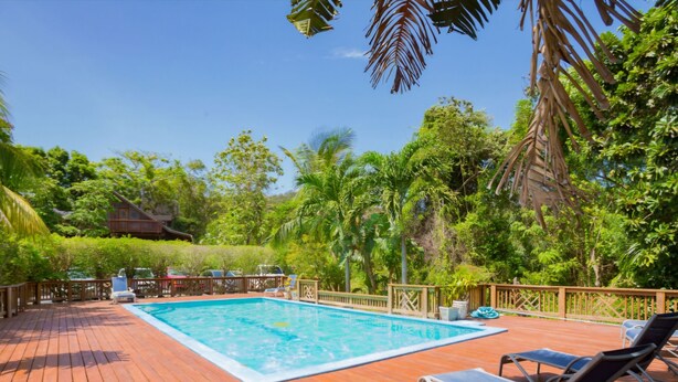 Um deck de madeira com piscina, cadeiras de descanso e cerca de madeira.