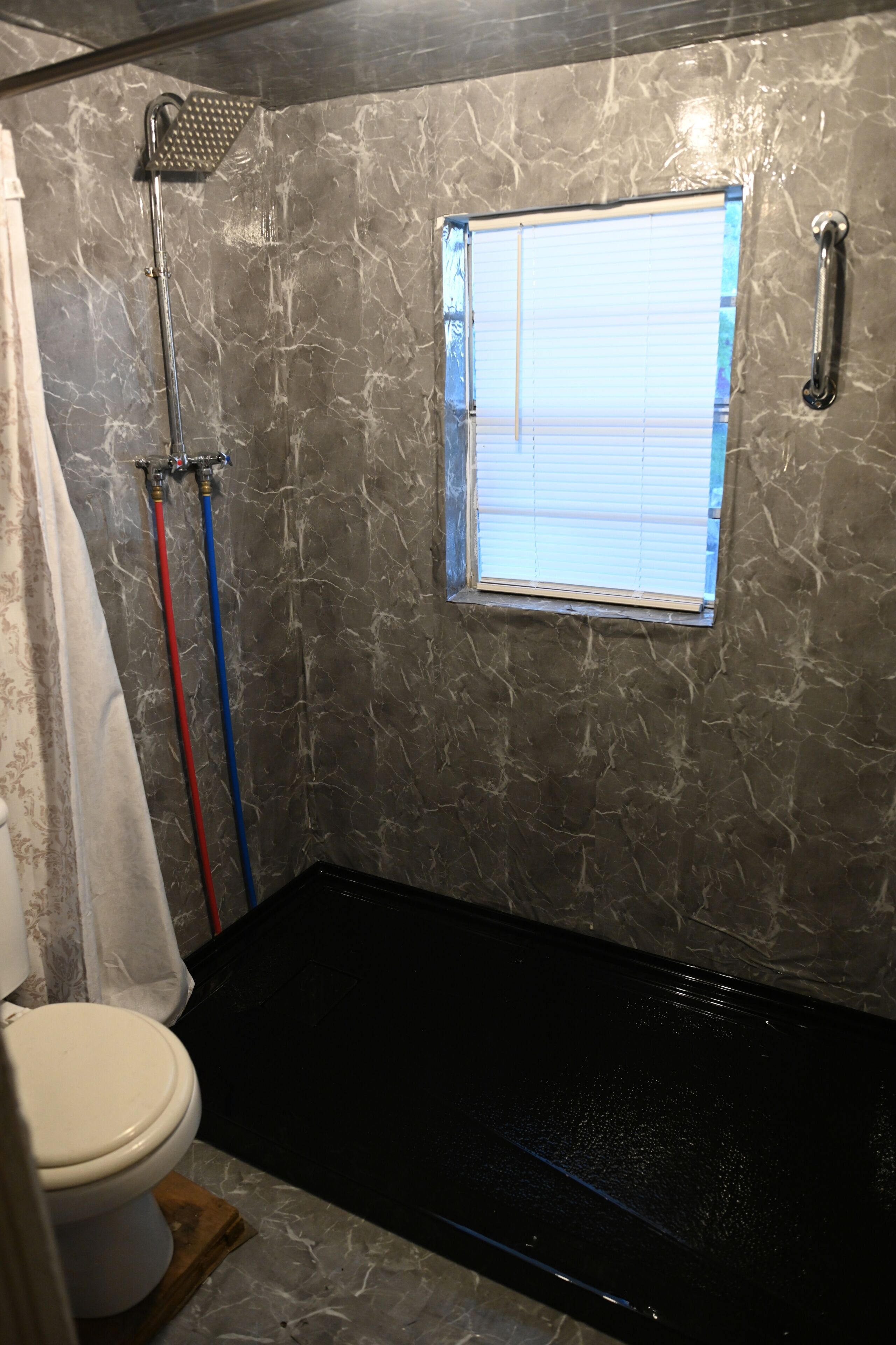 A bathroom with a shower, a toilet, and a window.