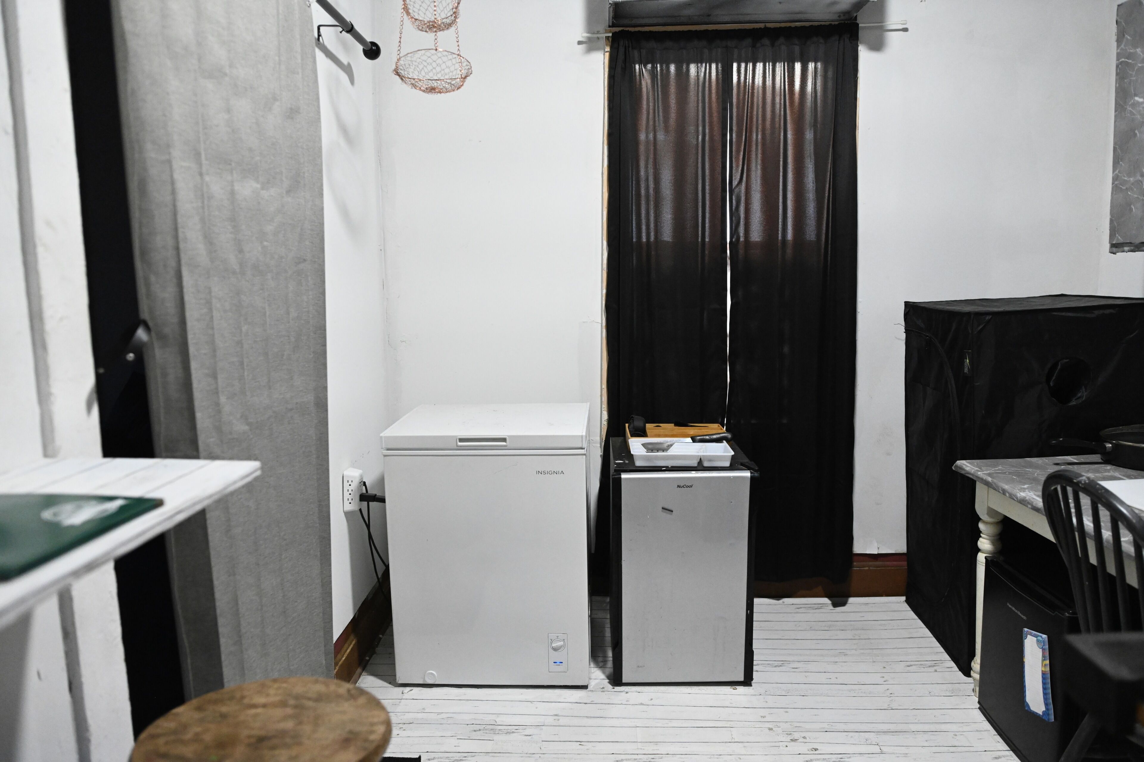 A compact kitchen with a white refrigerator, a smaller fridge, a wooden stool, and a black cabinet.
