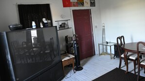 Una habitación con televisor, mesa de comedor de madera, sillas, una puerta roja y una estantería.