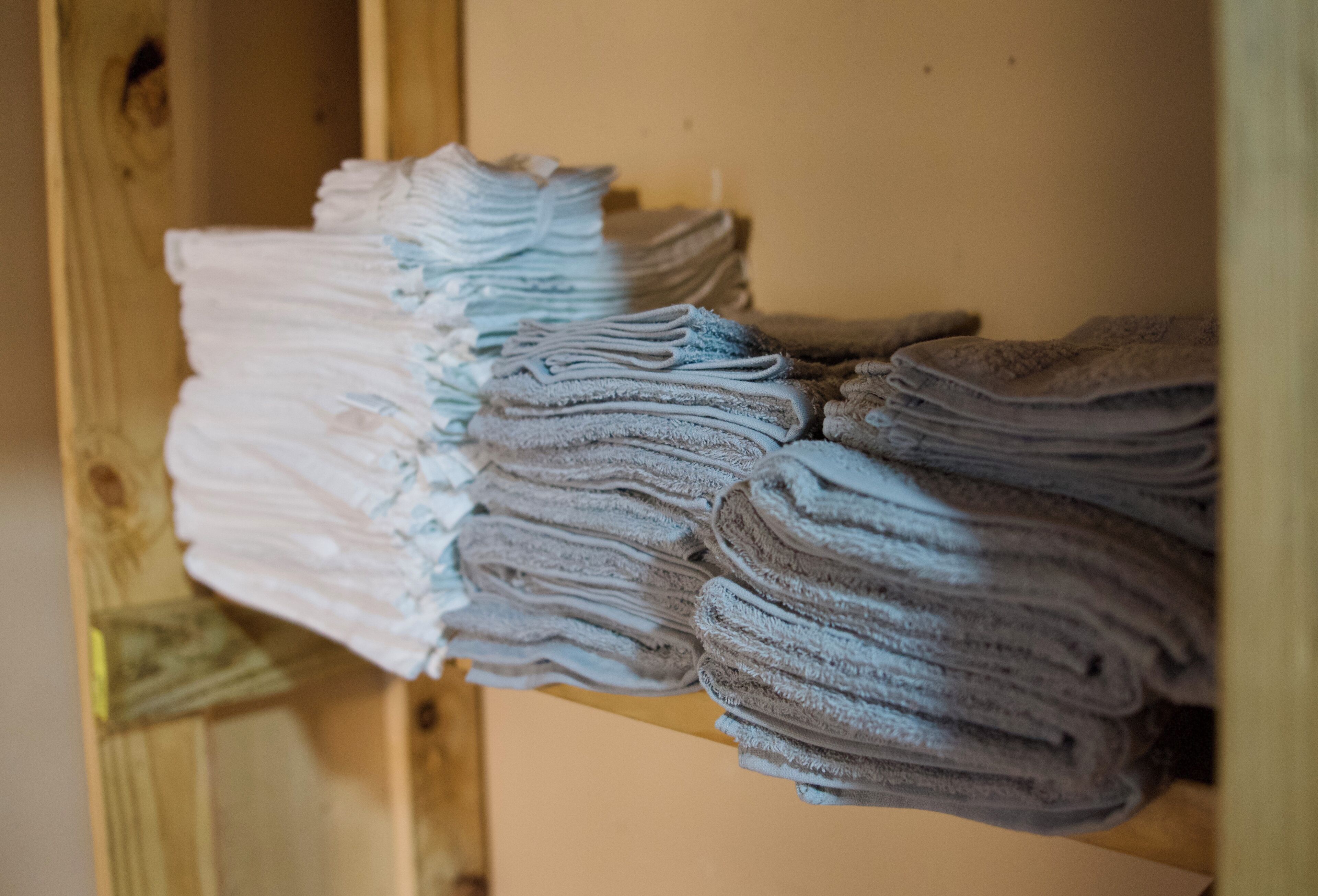 Un étagère en bois sur laquelle sont pliées avec soin des serviettes de différentes nuances de blanc et de gris.