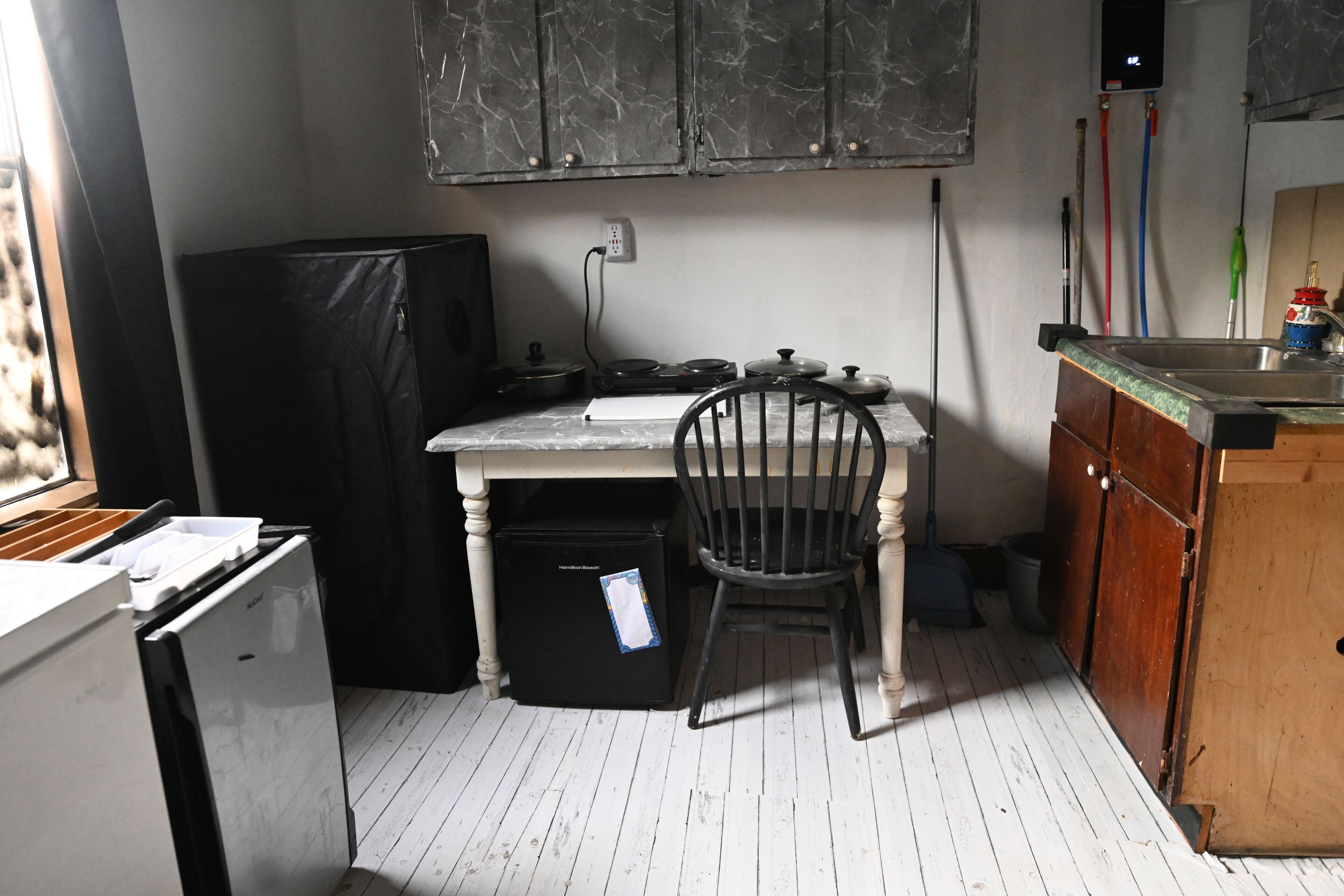 A compact kitchen with a refrigerator, a sink, a chair, and cabinets.
