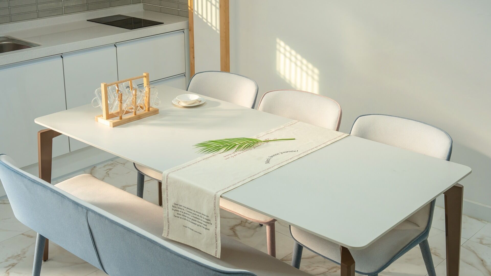 A modern kitchen with a white table, chairs, and a wooden rack with glasses.