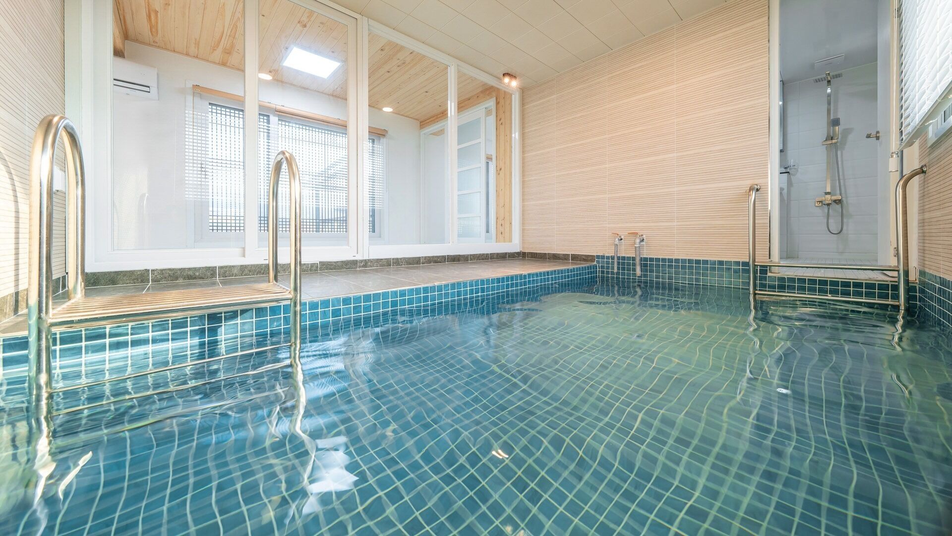 Una piscina interior con baldosas azules cristalinas, techo de madera y zona de duchas.