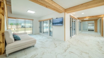 Una habitación de hotel moderna con piso de mármol, un sofá, un televisor y un baño visible a través de puertas de vidrio.