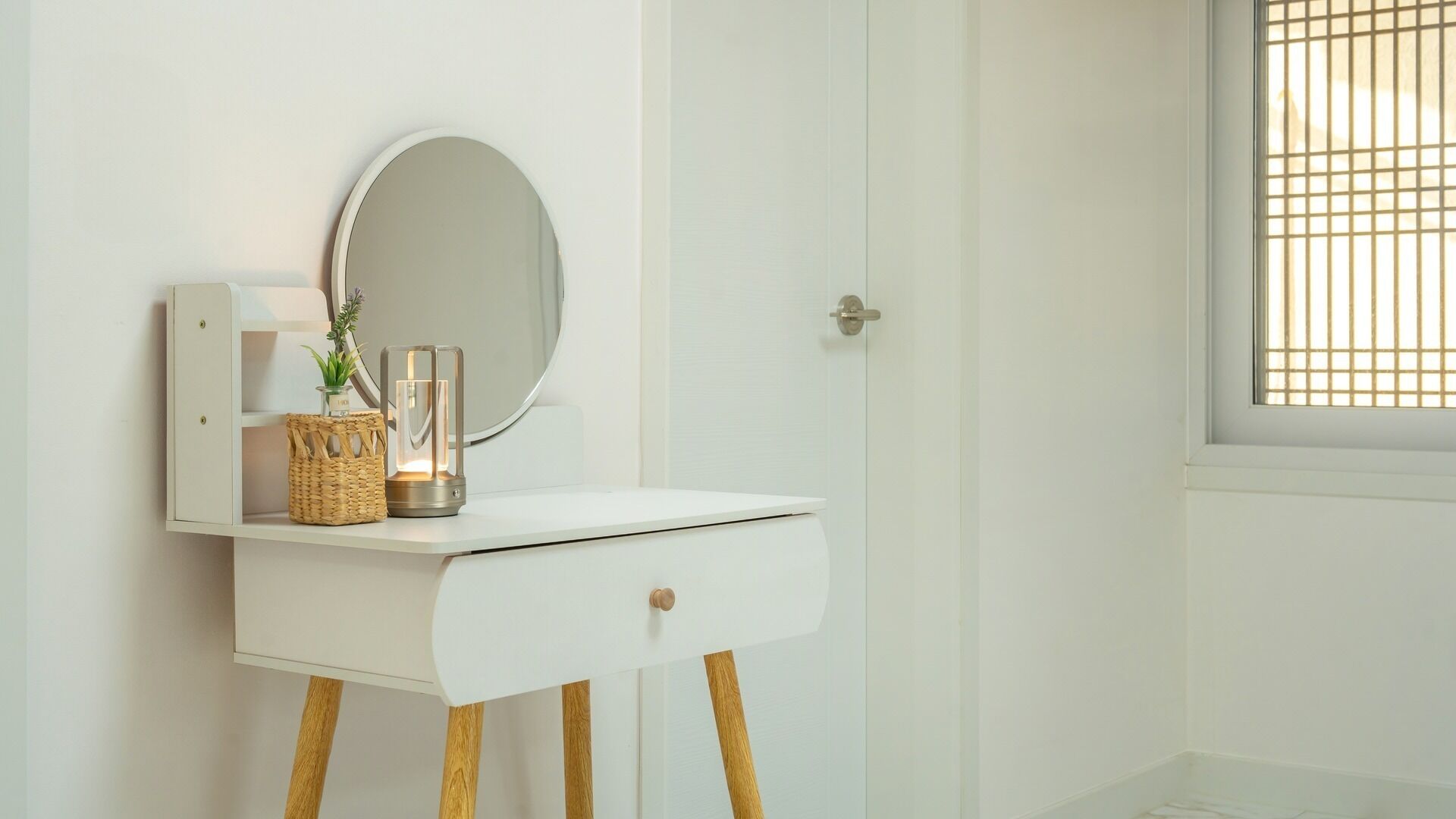 A white vanity with a round mirror, a small basket, and a candle.