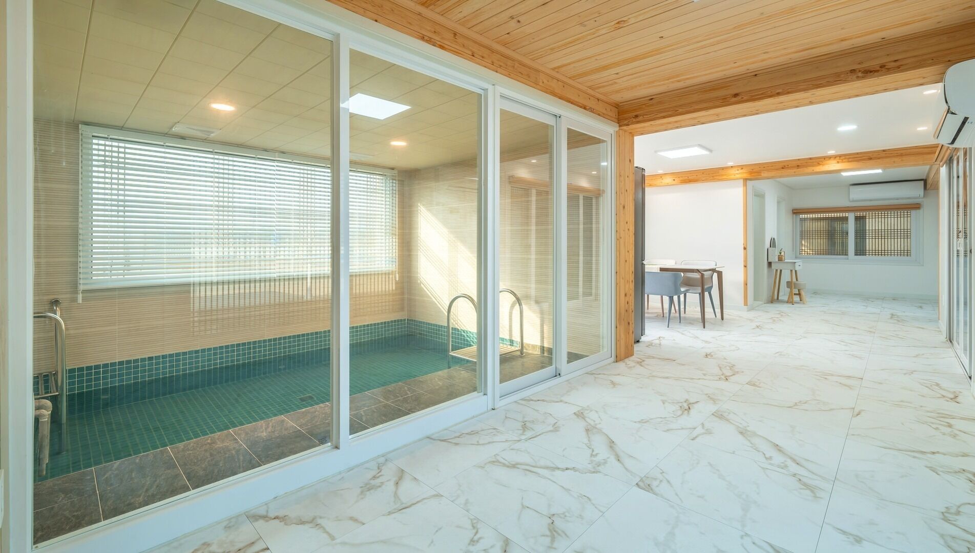 A modern interior with a swimming pool, sliding glass doors, a dining area, and a kitchen.