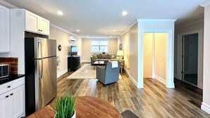 Una cocina moderna con refrigerador, estufa y gabinetes. Hay un comedor con mesa y sillas, y una sala de estar con sofá y mesa auxiliar.