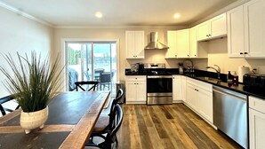 Una cocina moderna con armarios blancos, una mesa de comedor de madera y vistas a través de la puerta de vidrio.