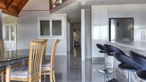 A modern kitchen with a glass dining table, wooden chairs, and a stainless steel refrigerator.