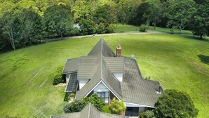 A house with a sloped roof, surrounded by a large green lawn and dense trees.