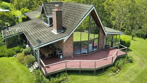 A modern house with a large deck, a chimney, and a glass conservatory.