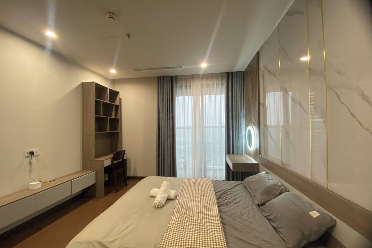 Quarto de hotel moderno com uma cama grande, um guarda-roupa embutido, uma toucador com espelho e uma janela ampla com cortinas.